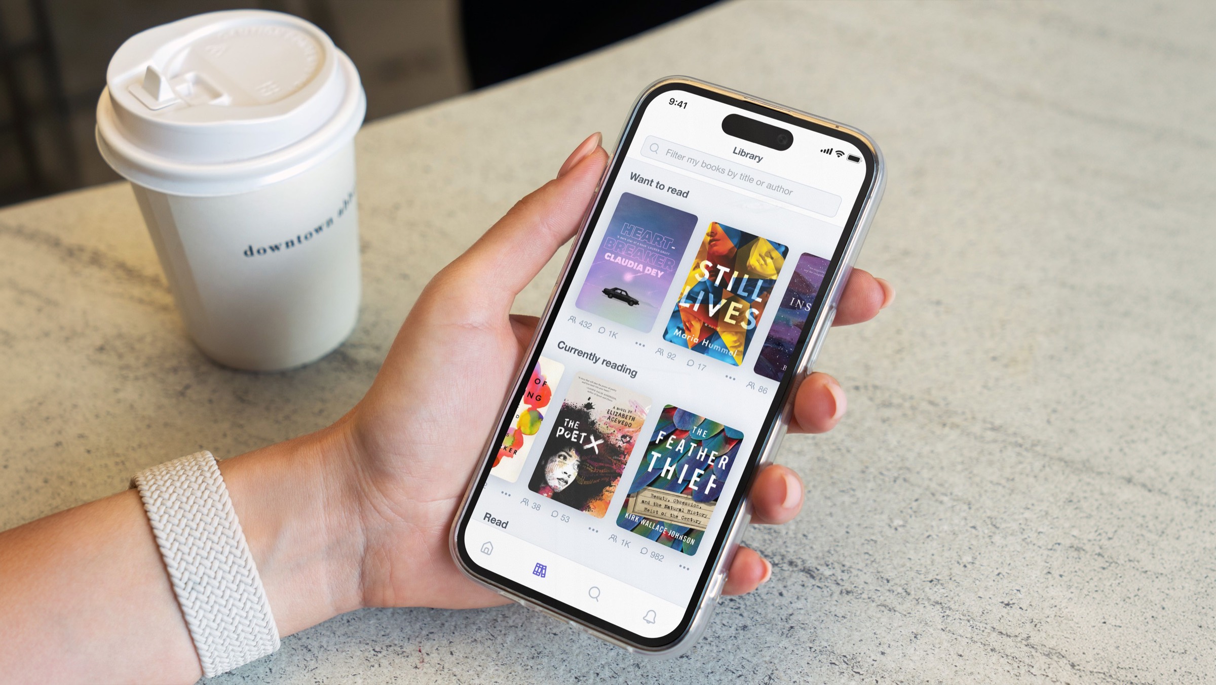 En hånd som holder en telefon som viser et Byzans-bibliotek av bokomslag, ved siden av en kaffekopp